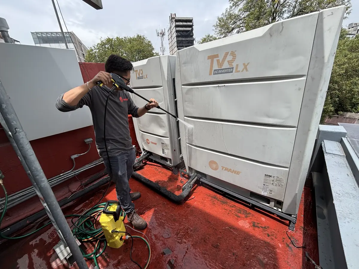 Técnico lavando a presión una condensadora Trane VRF en una azotea
